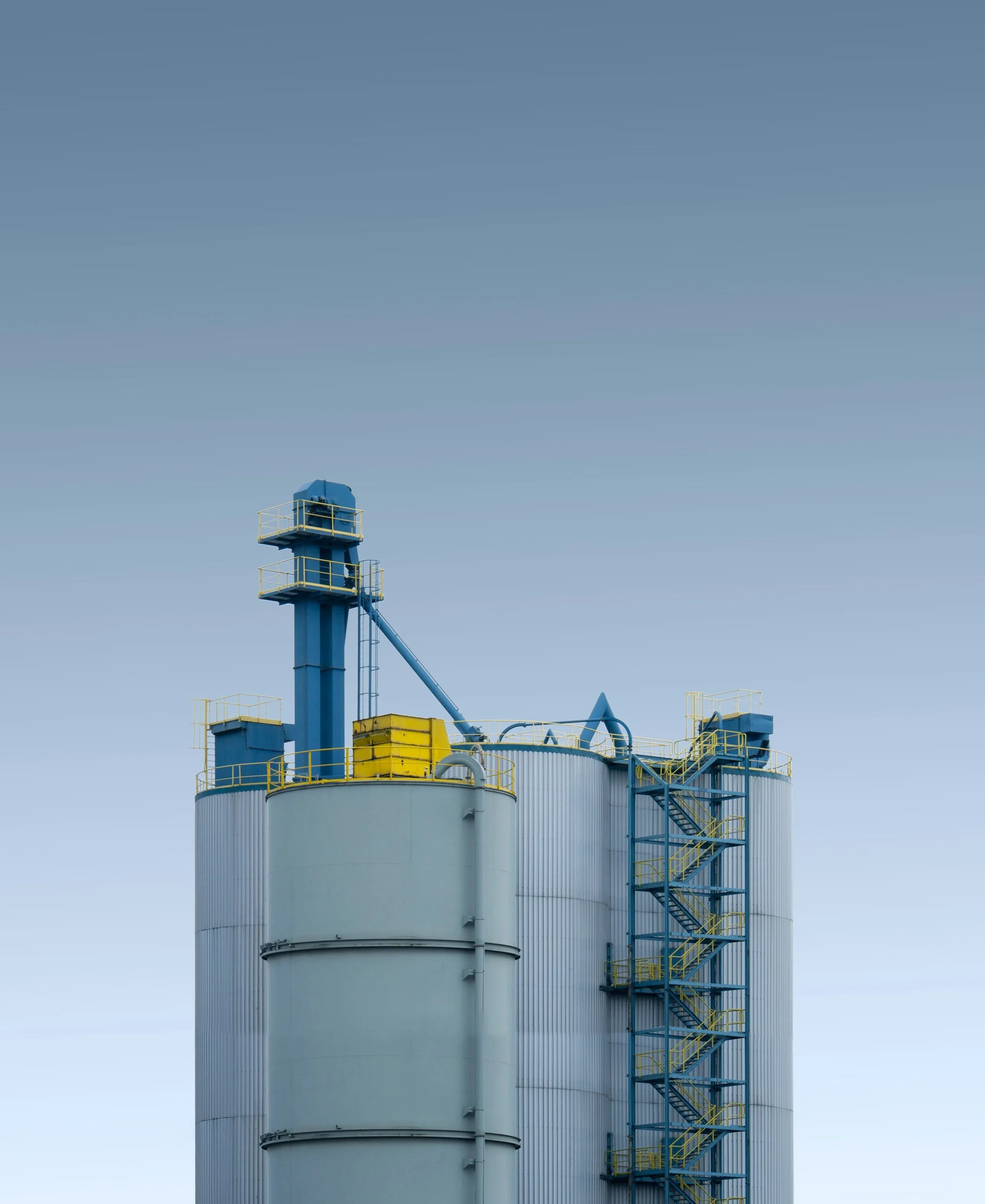 Siloturm für Schüttgut mit blauem Becherwerk vor klarem Himmel.